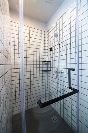 A small, tiled shower stall with a handheld showerhead, a toilet, and a shelf with toiletries. - Suisse Place Shanghai (Shanghai)