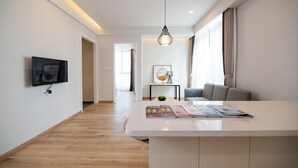 A modern living room with a flat-screen TV, a central island with magazines, a hanging light fixture, and a sofa. - Suisse Place Shanghai (Shanghai)