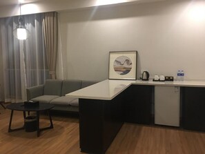 A compact living space with a sofa, a small table, a kitchenette, and a framed picture on the wall. - Suisse Place Shanghai (Shanghai)