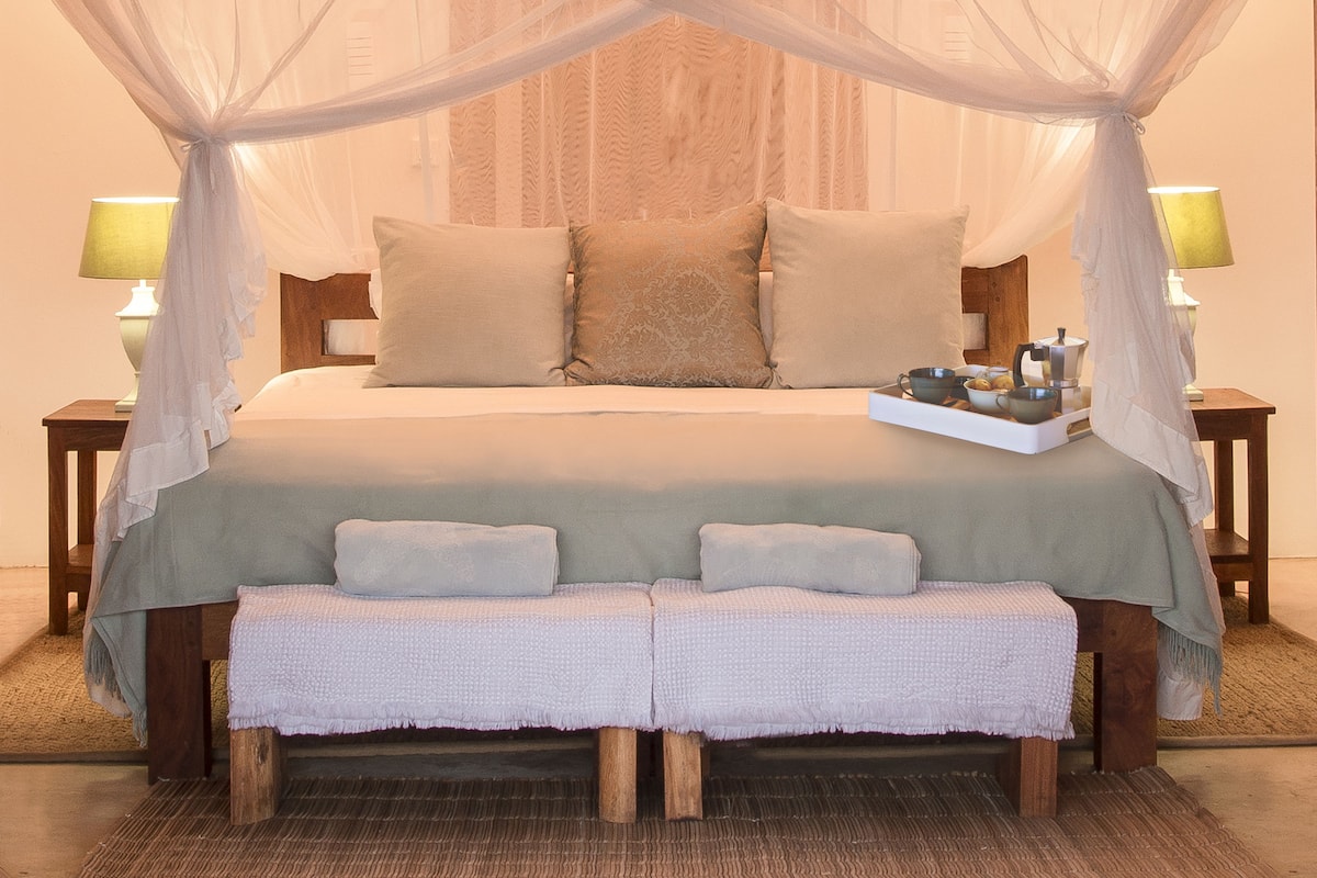 A bed with a canopy, two bedside tables with lamps, and a tray of toiletries.