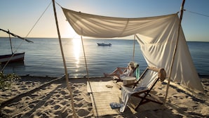 Une plage avec un auvent, un bateau et une personne se relaxant sur une chaise.
