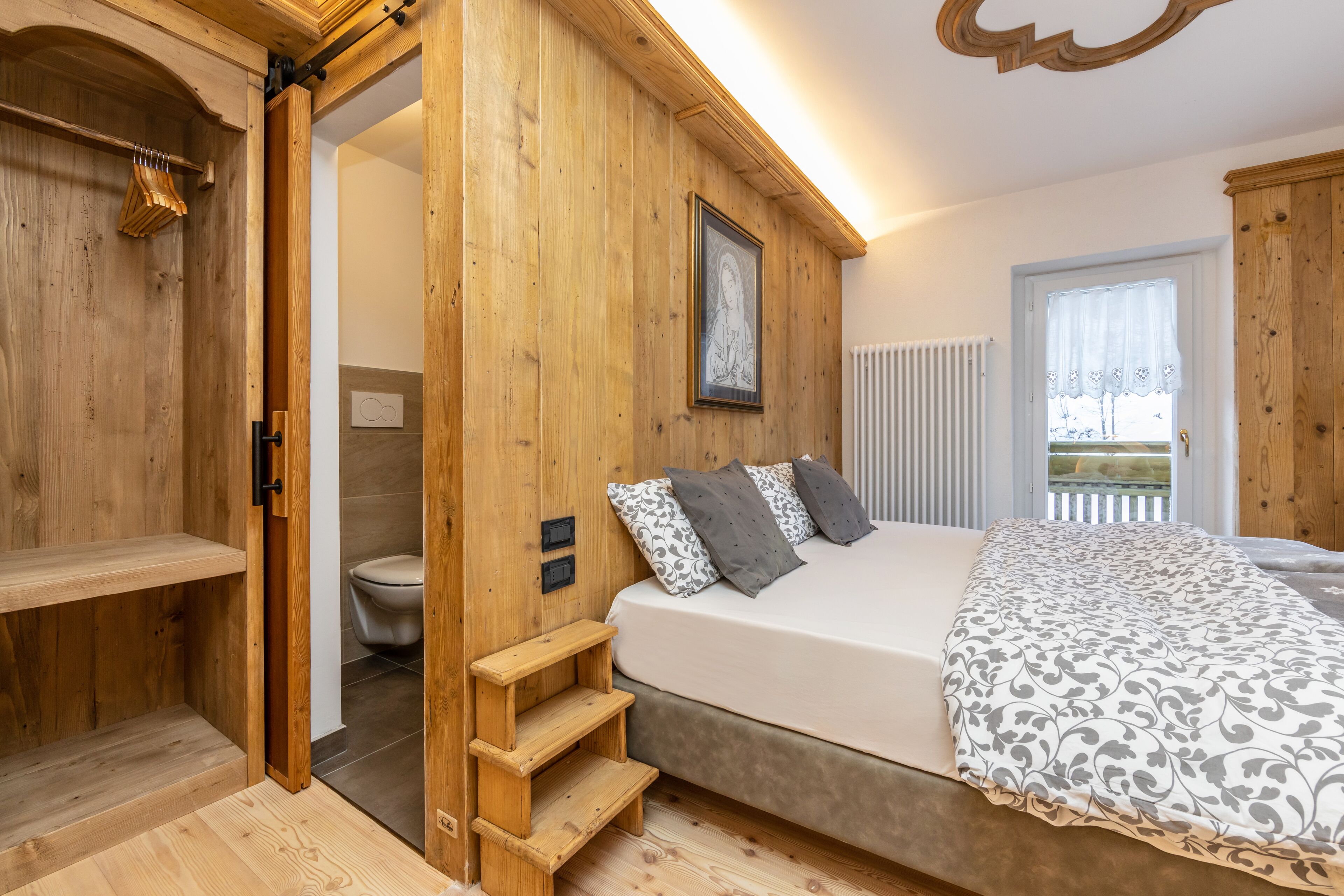 Ein Zimmer mit Holzboden, einem Bett, einem Holzbodenregal und einer Tür zu einem Badezimmer.