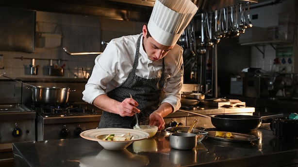 A chef in a professional kitchen with stainless steel appliances and a variety of cooking utensils. - Rifugio Cereda (Primiero San Martino di Castrozza)