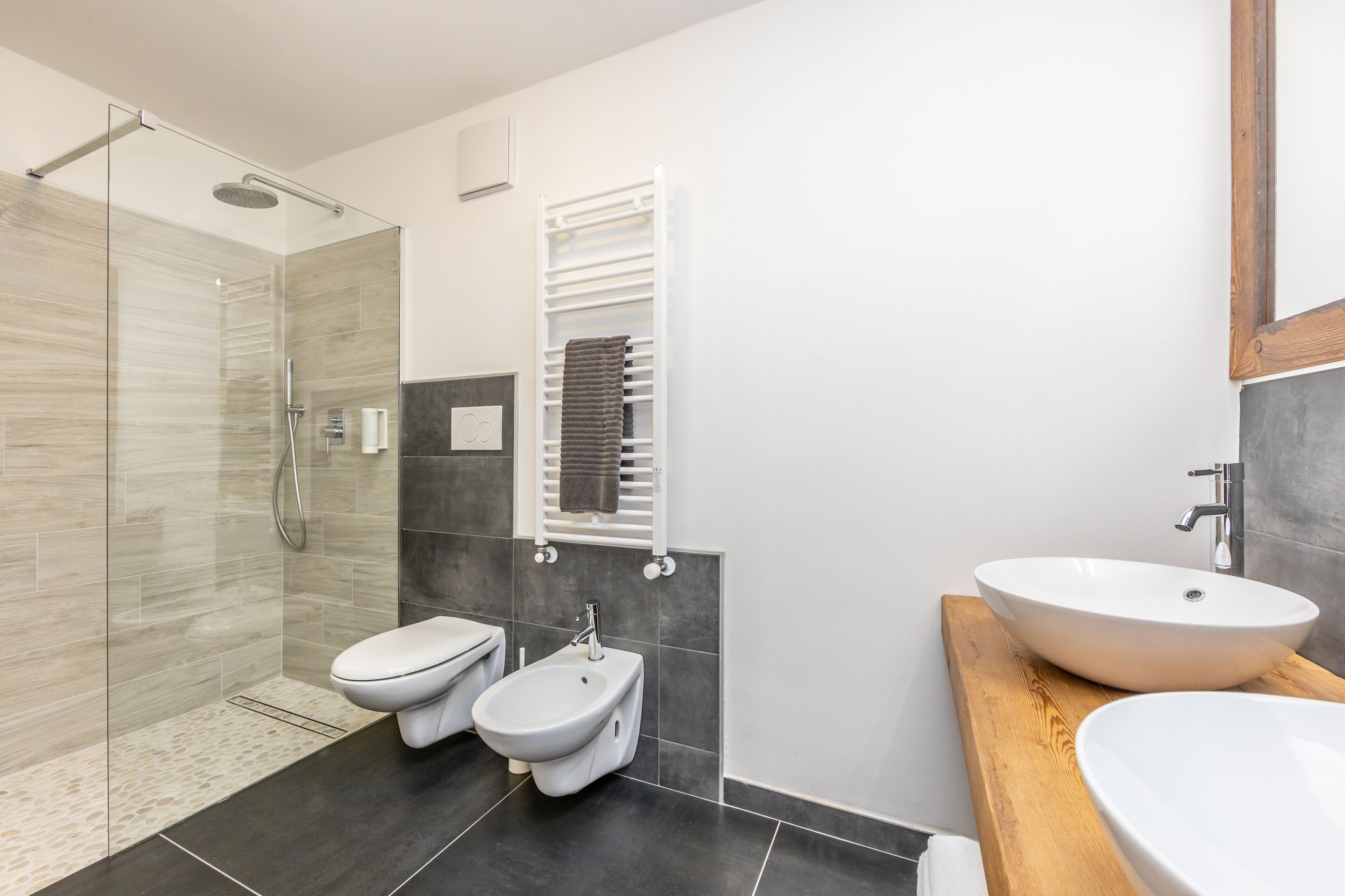 A modern bathroom with a glass shower enclosure, a bidet, a toilet, and a large vessel sink.