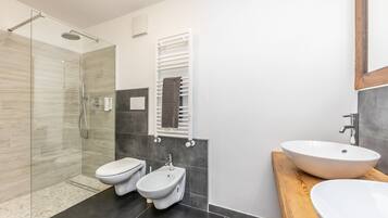 A modern bathroom with a glass shower enclosure, a bidet, a toilet, and a large vessel sink.