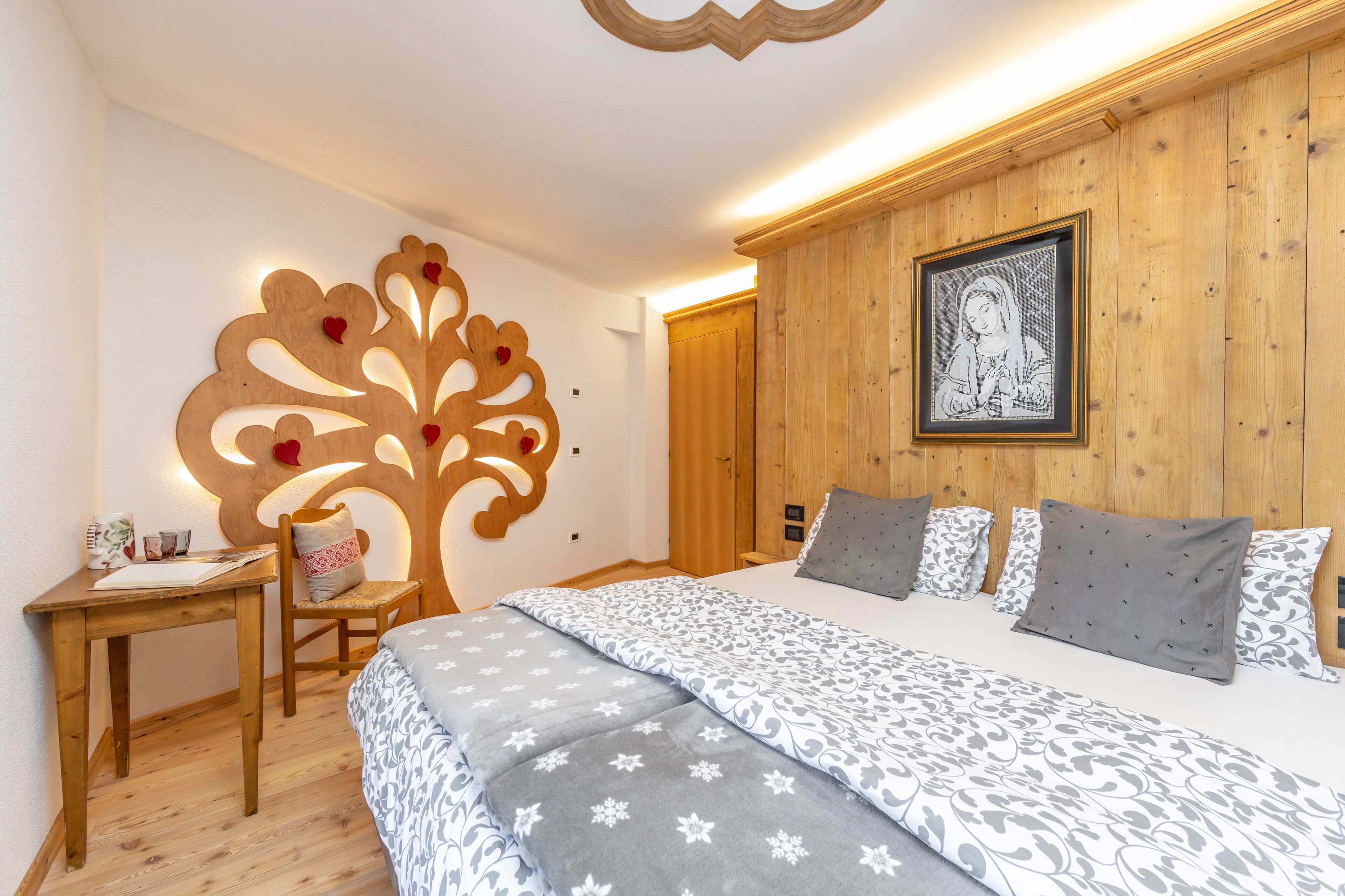 A bedroom with a wooden headboard, a bed with patterned bedding, a desk with a chair, and a wall decoration.