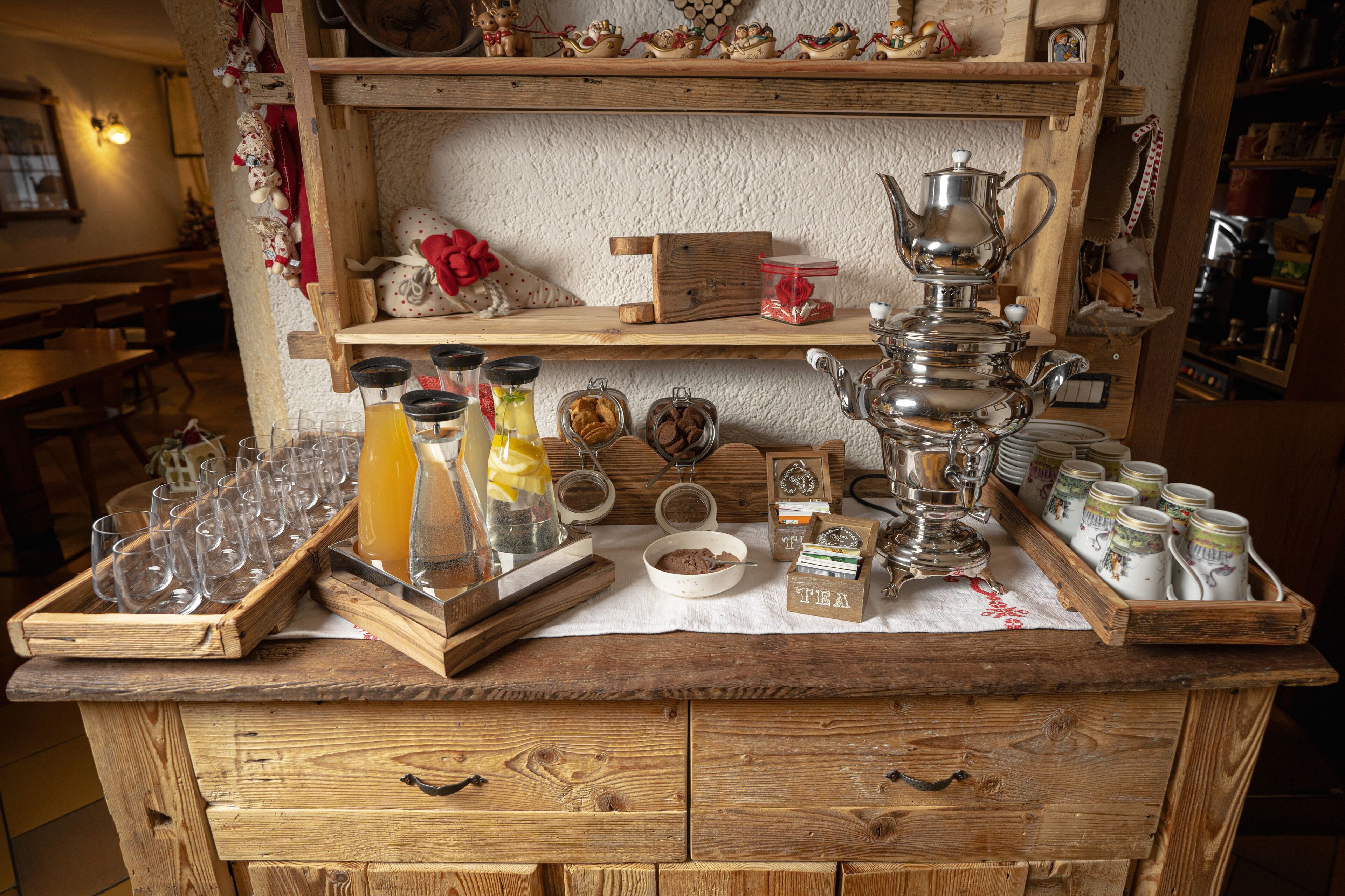 Een houten toog met drinkglaasjes, een koffiepers en theeblikken.