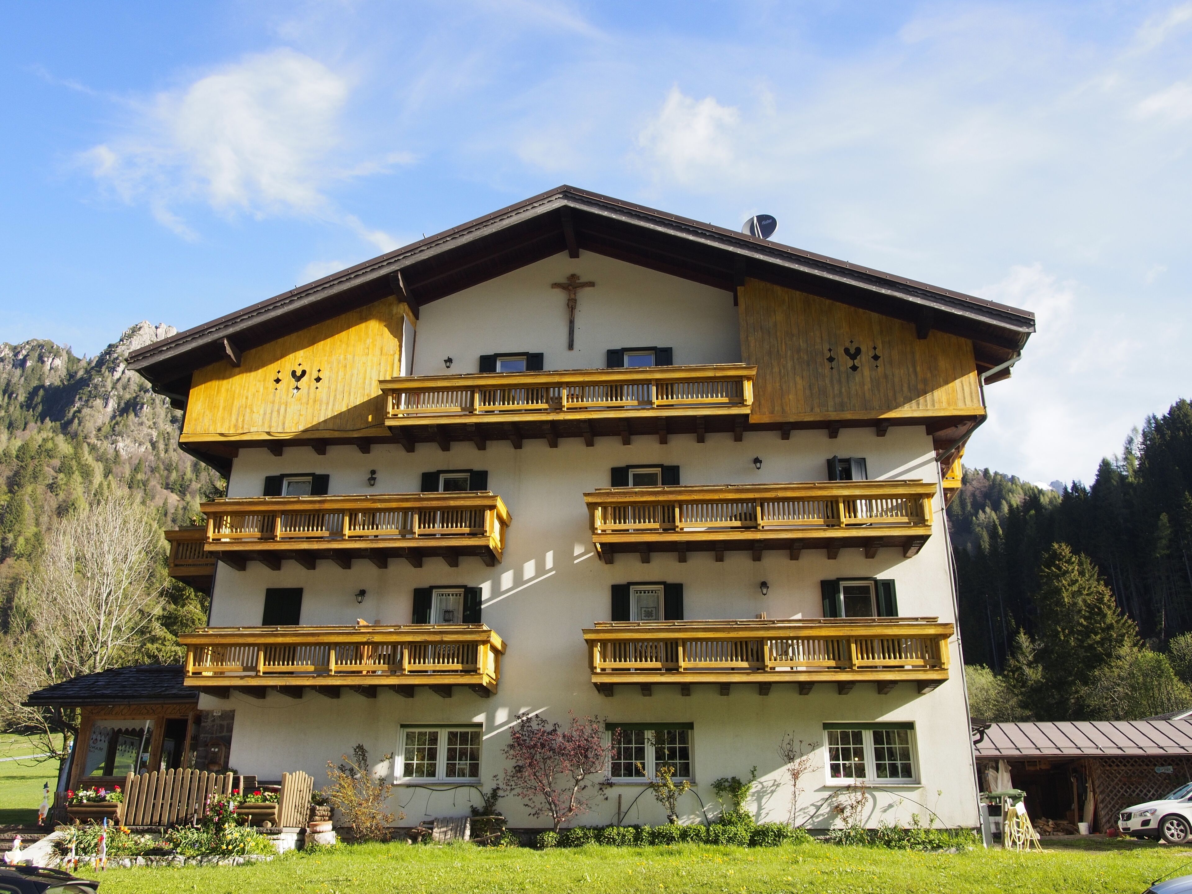 Un edificio de varios pisos con balcones de madera, una cruz en la fachada y montañas al fondo.