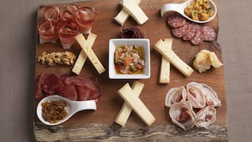 Ein Holzbrett mit verschiedenen Käsesorten, Wurstwaren und einer kleinen Schale Essiggurken.