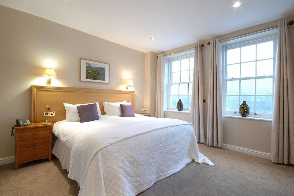 Een hotelkamer met een groot bed, twee bedlampen, een nachtkastje en een raam met gordijnen.