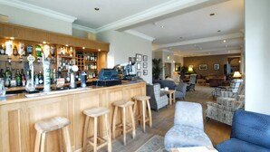 Een bar met krukken, een koffieapparaat en verschillende flessen drank.