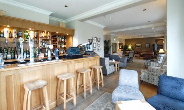 Uma área de bar com banquetas, uma máquina de café e diversas garrafas de bebidas alcoólicas.