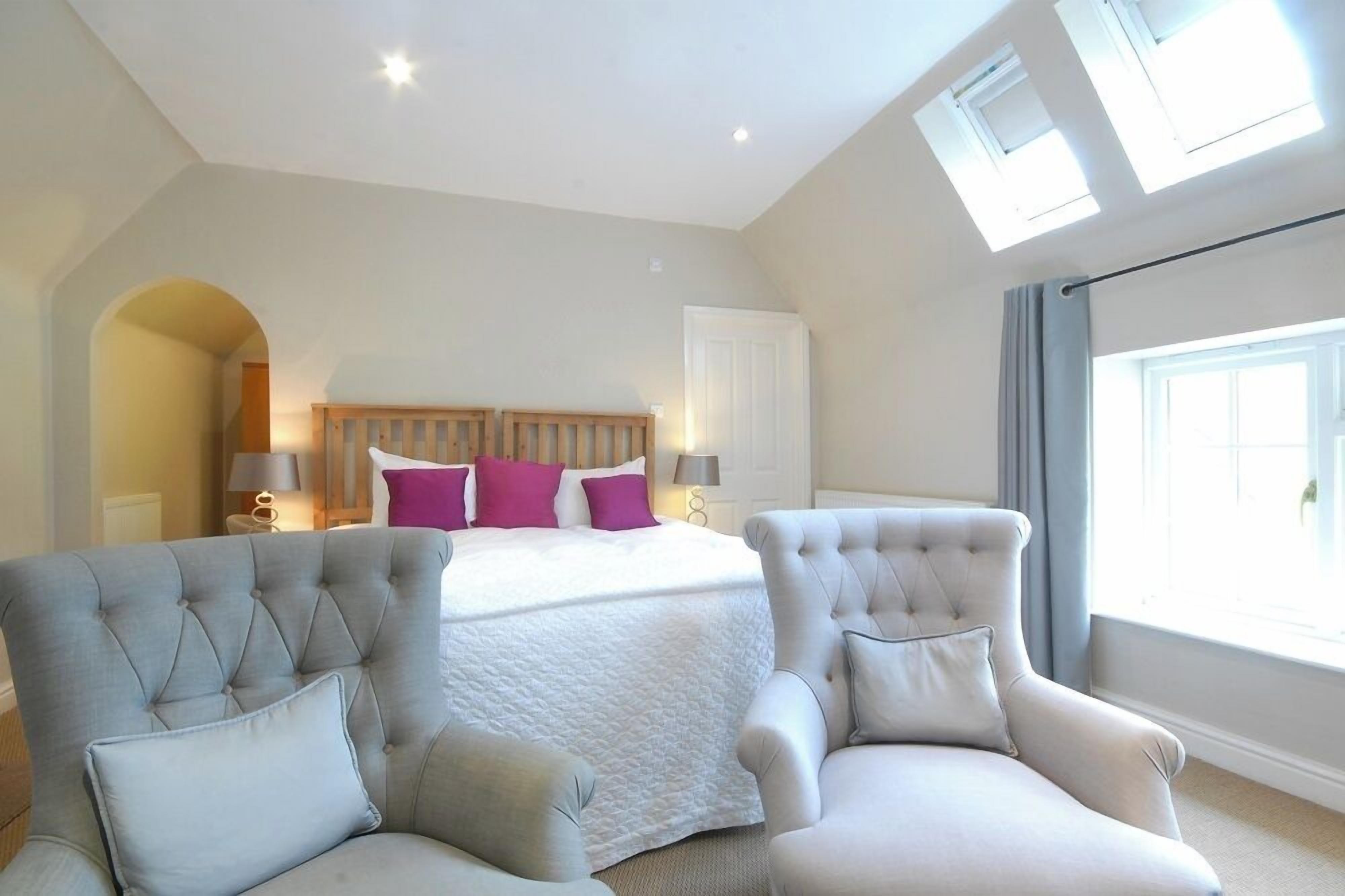 Een slaapkamer met een bed, twee fauteuils, een dakraam en een groot raam.