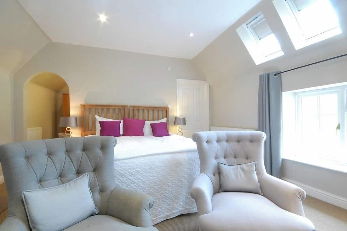 Een slaapkamer met een bed, twee fauteuils, een dakraam en een groot raam.