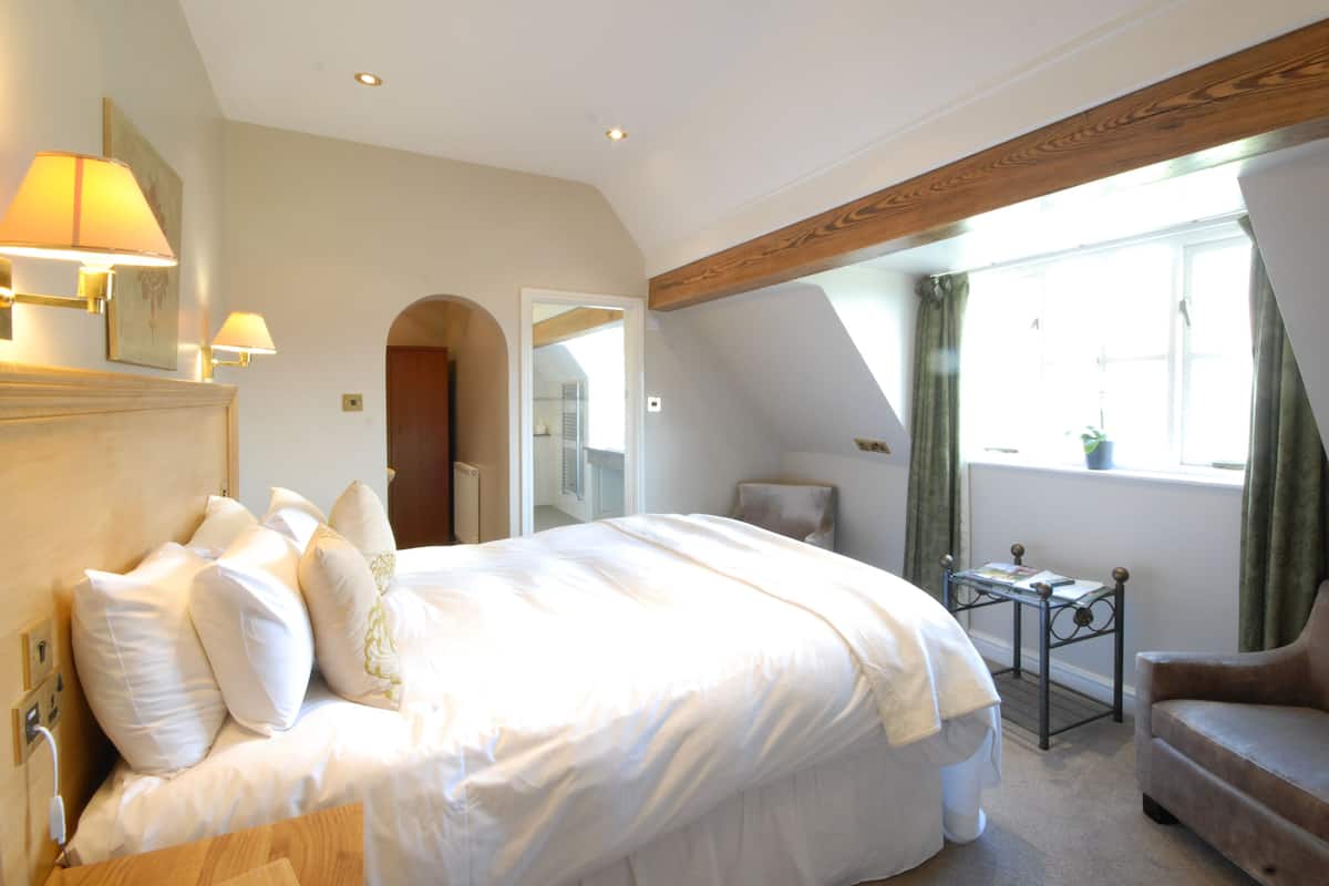 Een slaapkamer met een groot bed, een klein tafeltje, een stoel en een raam met gordijnen.