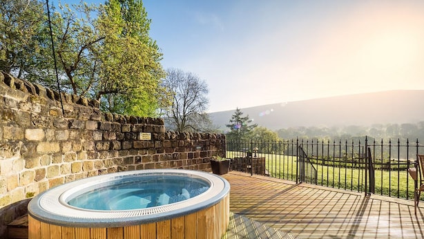 Een hottub op een houten terras, met een stenen muur en uitzicht op een gazon.