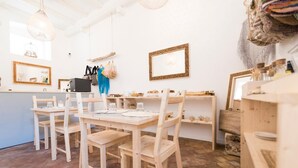A dining area with wooden tables and chairs, a brick floor, and a white interior. - Casa Maritrì (Pachino)