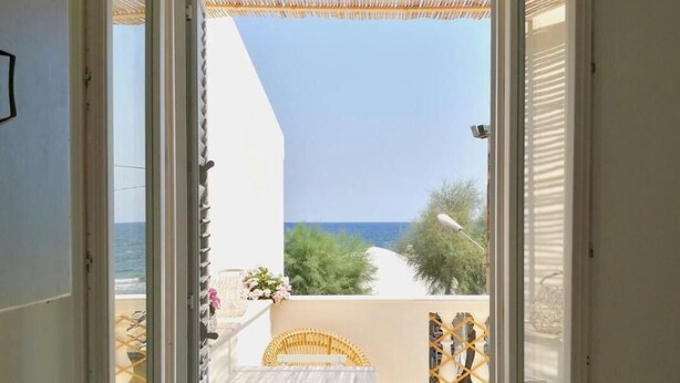 A sliding glass door leading to an outdoor patio with a table and chairs, a wicker chair, and a hanging light fixture. - Casa Maritrì (Pachino)