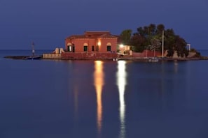 A coastal building with a waterfront view, a lighthouse in the background, and a calm sea. - Casa Maritrì (Pachino)