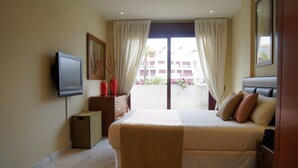 A hotel room with a bed, a television, a window with curtains, and a view of the outside building. - Parque Botanico Resort & Country Club (Benahavis)