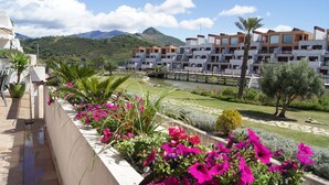 A balcony with vibrant flowers, a view of a modern apartment building, and a mountainous landscape in the background. - Parque Botanico Resort & Country Club (Benahavis)