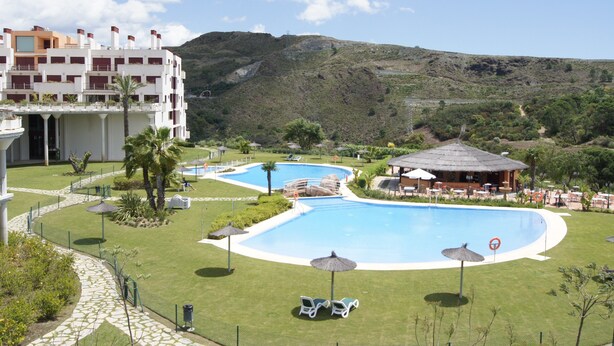 A resort with a large swimming pool, lounge chairs, and a building with multiple balconies. - Parque Botanico Resort & Country Club (Benahavis)