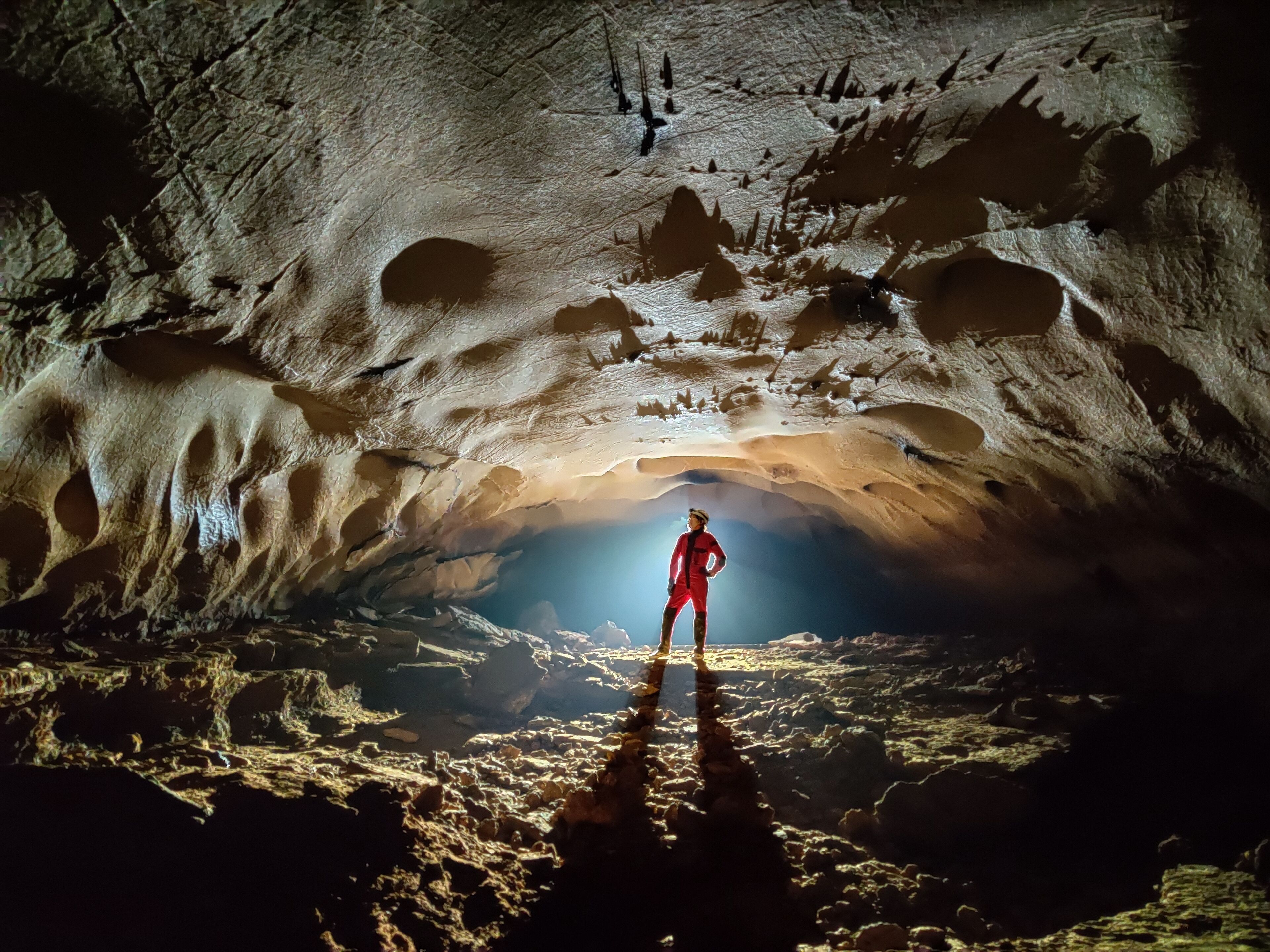 A person standing in a cave with a large opening at the end.