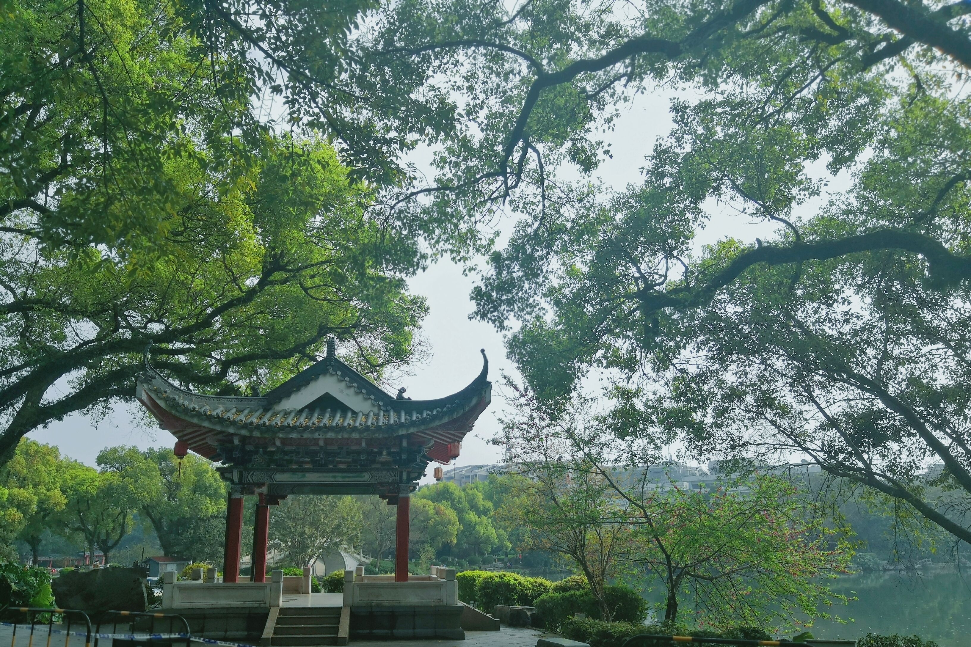A traditional pavilion with a curved roof, surrounded by lush greenery and trees.