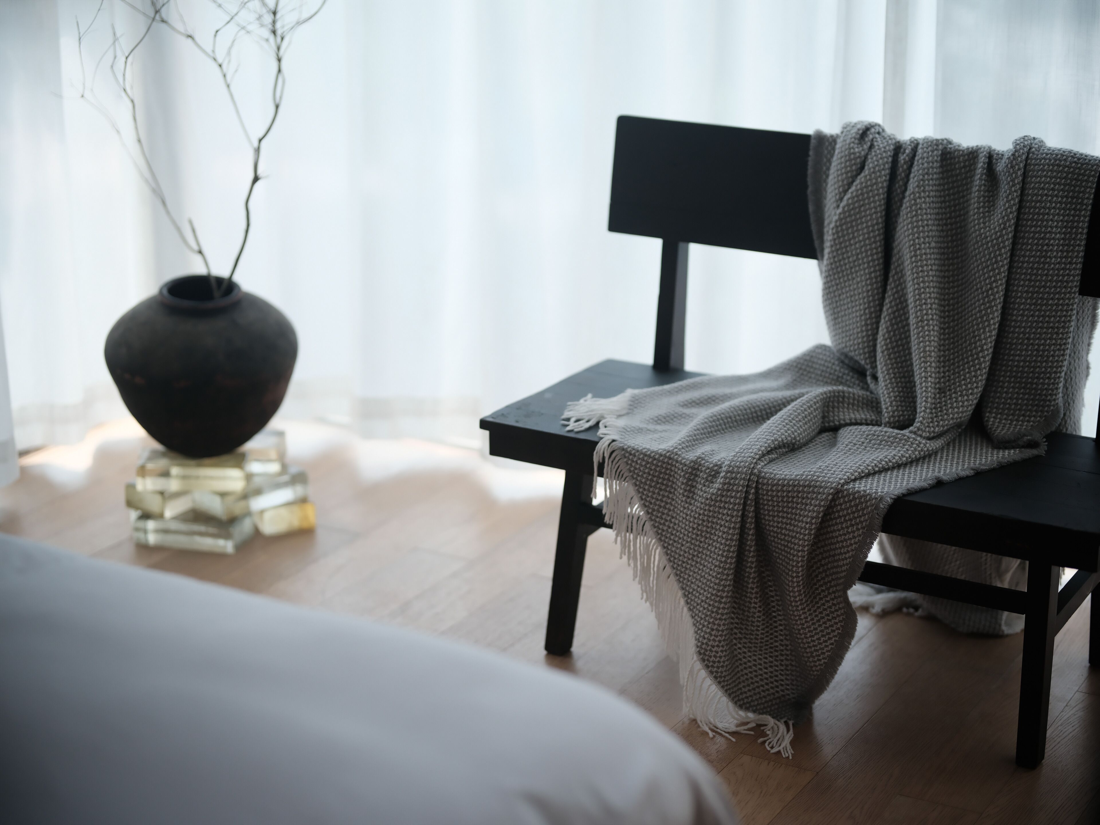 Una habitación moderna con una silla negra, un sofá blanco y un jarrón decorativo sobre una mesa de cristal.