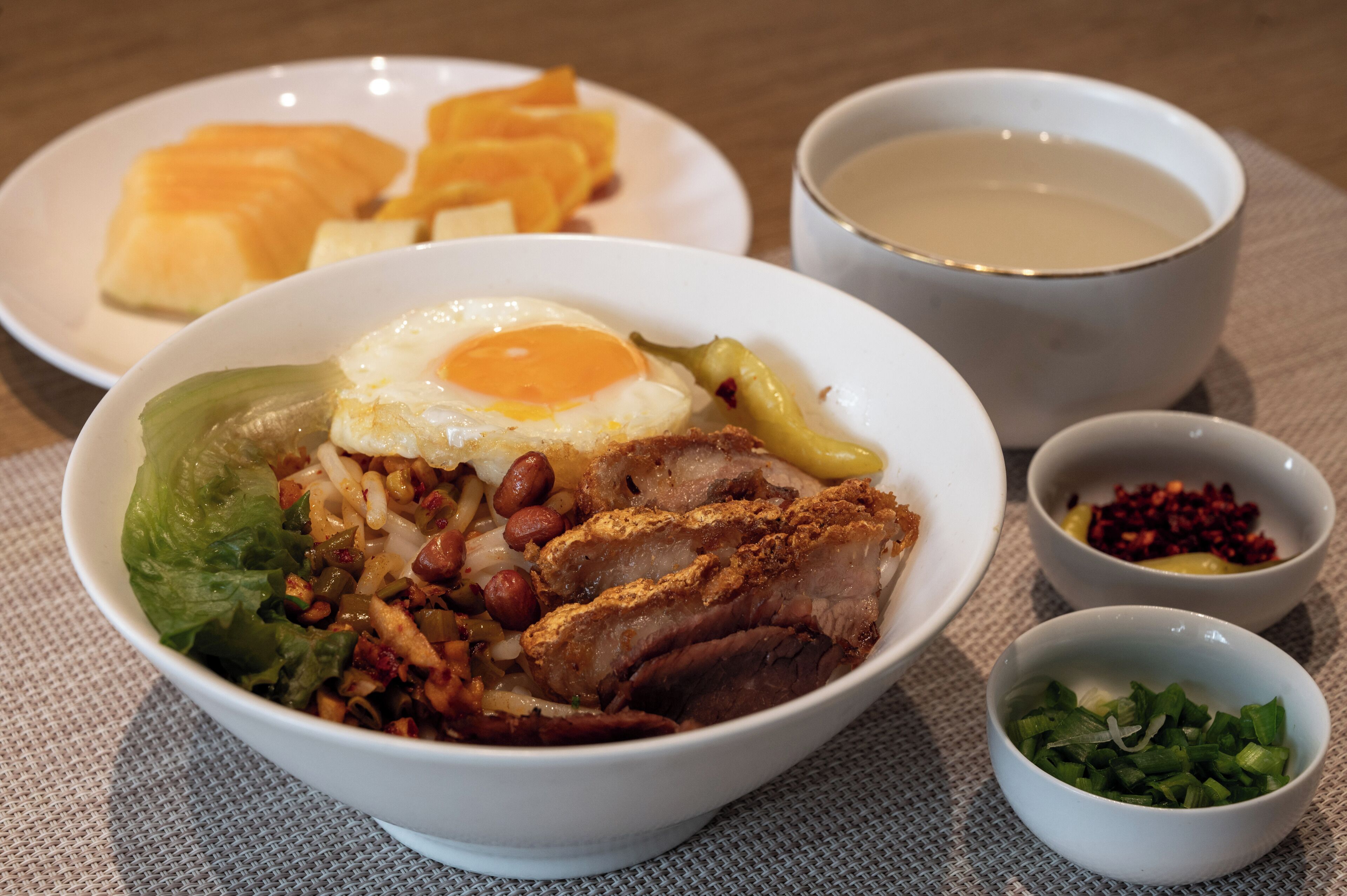 Un repas composé d’un œuf au plat, de viande et de légumes servis sur une assiette, accompagné d’un bol de soupe et de petits bols contenant des condiments.