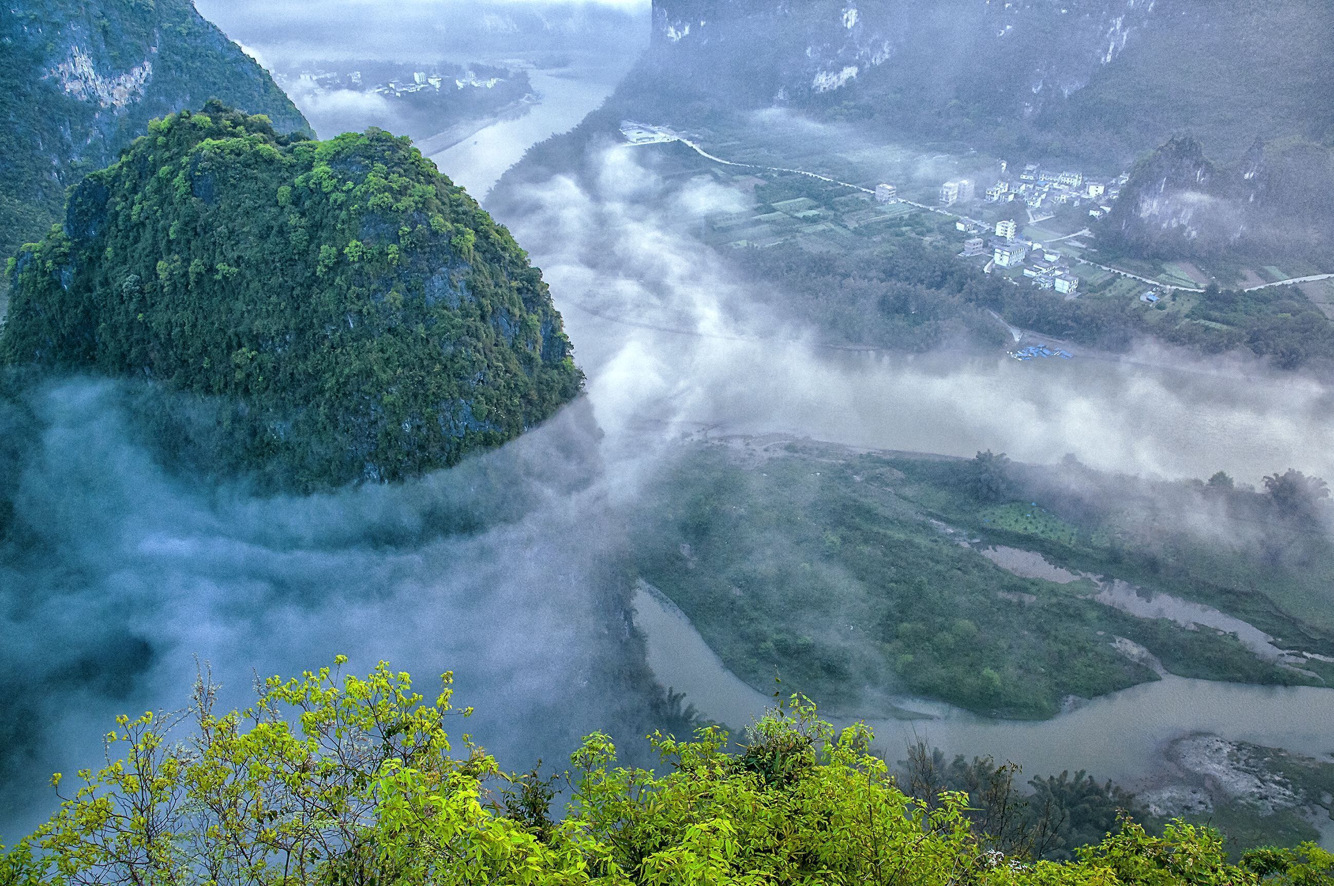 Un paysage montagneux avec une rivière, une forêt dense et un petit village.