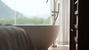 A modern bathroom with a freestanding bathtub, a showerhead, and a view of a mountainous landscape through a large window. - Guilin Bonjour Boutique Hotel (Guilin)