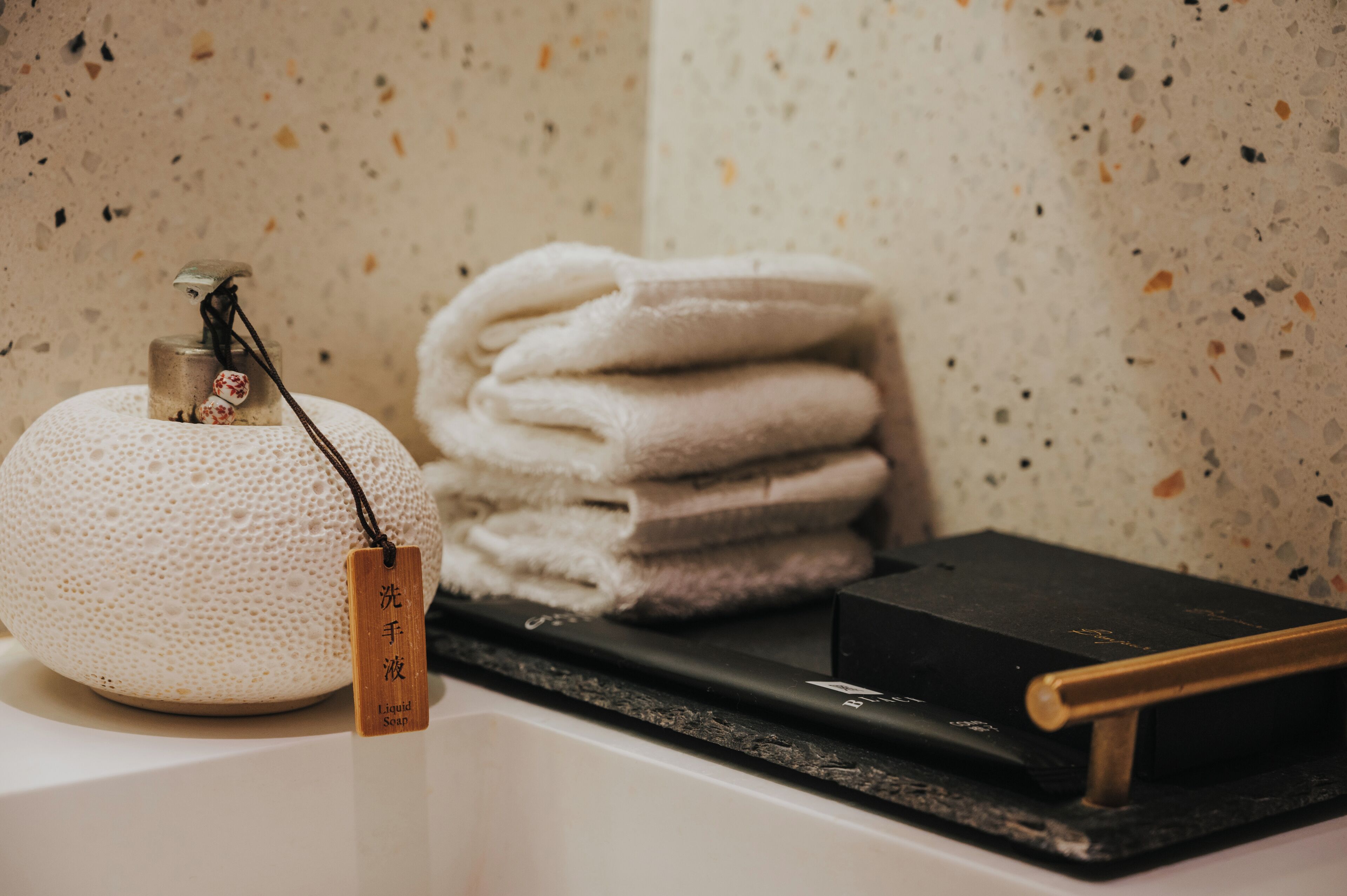 A bathroom with a soap dispenser, a stack of towels, and a black object on the counter.