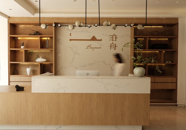 A reception desk with a laptop, wooden shelves with decorative items, and a sign with 'Bonjour' and Chinese characters. - Guilin Bonjour Boutique Hotel (Guilin)