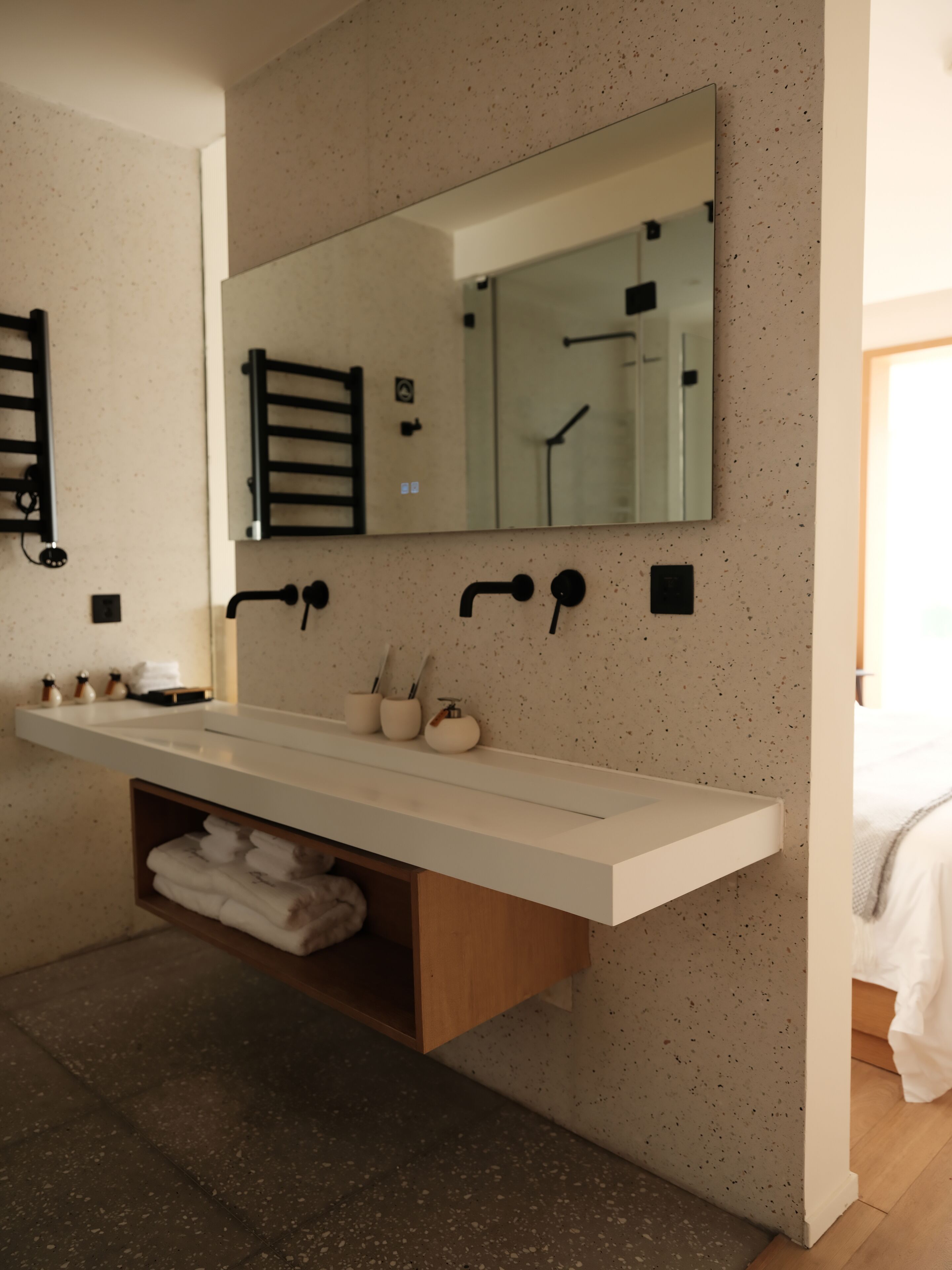 A modern bathroom with a white vanity, a large mirror, and a towel shelf.