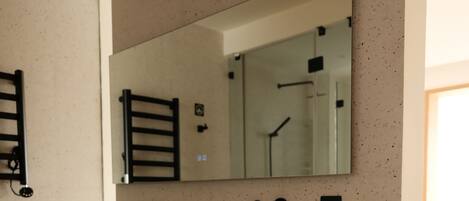 A modern bathroom with a white vanity, a large mirror, and a towel shelf.