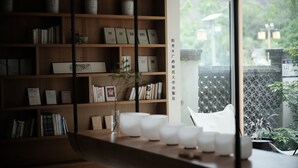 A modern interior with wooden shelves displaying books and tea containers. A white table with cups and a vase is in the foreground. - Guilin Bonjour Boutique Hotel (Guilin)