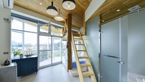 Un intérieur moderne avec un plafond en bois, une grande fenêtre donnant sur la ville, une échelle et un coin cuisine.