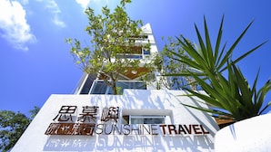 Un bâtiment avec une enseigne indiquant « Sunshine Travel » et un arbre devant.