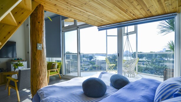 Une chambre moderne avec un grand lit, un plafond en bois et une vue sur la ville grâce à de grandes fenêtres.
