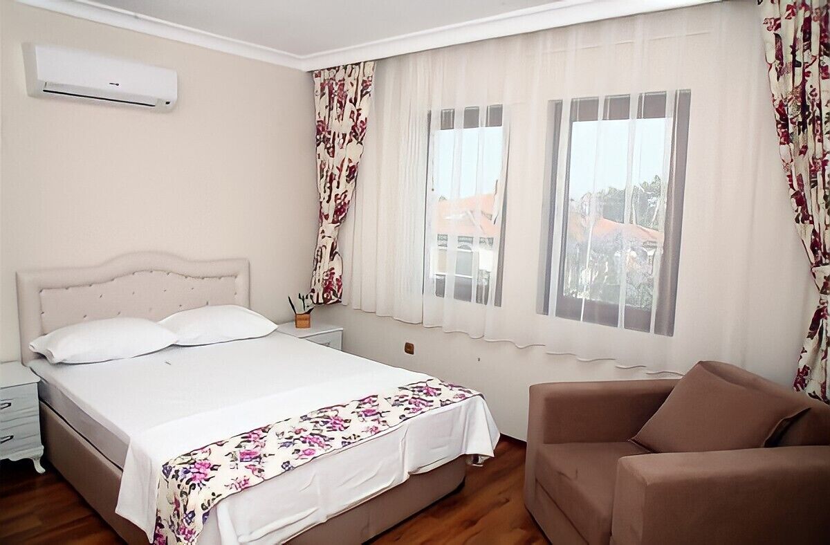 Une chambre à coucher avec un lit, une table de chevet, une chaise et une fenêtre avec des rideaux.