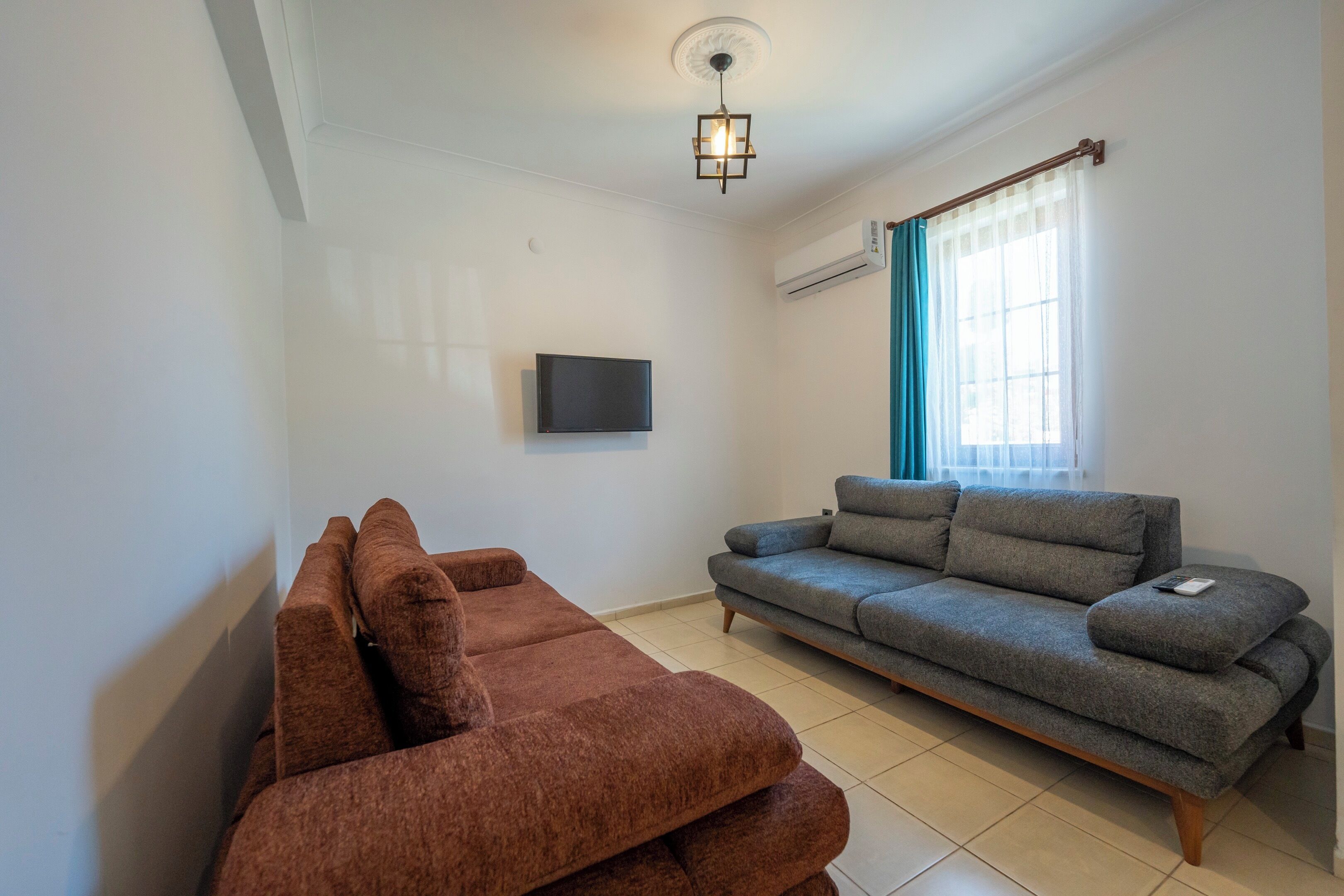 A living room with a brown sofa, a grey sofa, a flat-screen TV, and a ceiling light fixture.
