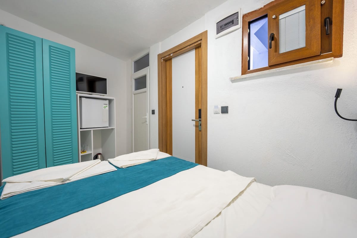 A bedroom with a bed, a wardrobe, a small shelf, and a door.