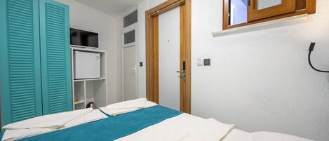 A bedroom with a bed, a wardrobe, a small shelf, and a door.