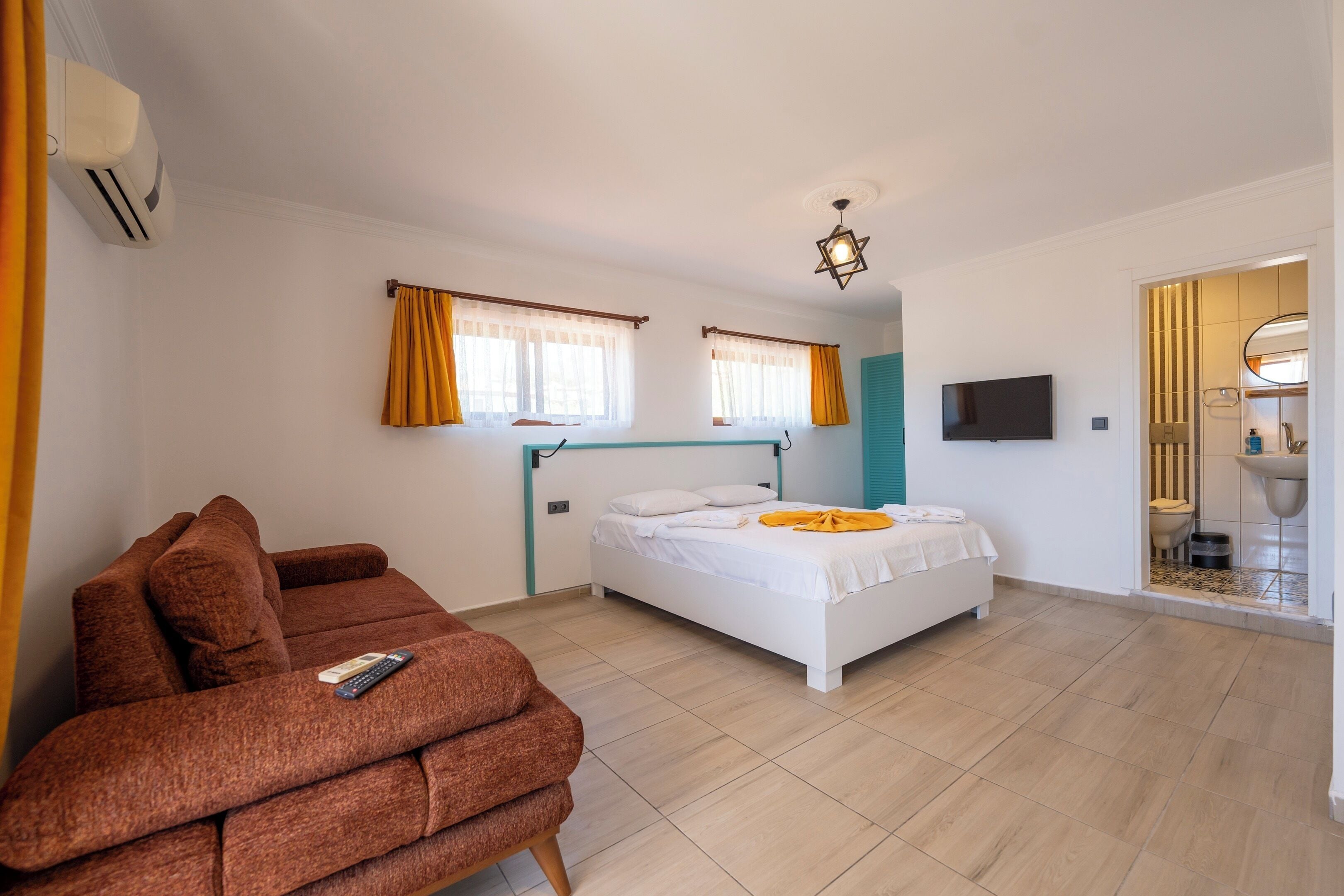 Un dormitorio con cama, sofá, televisión y baño visible a través de una puerta abierta.