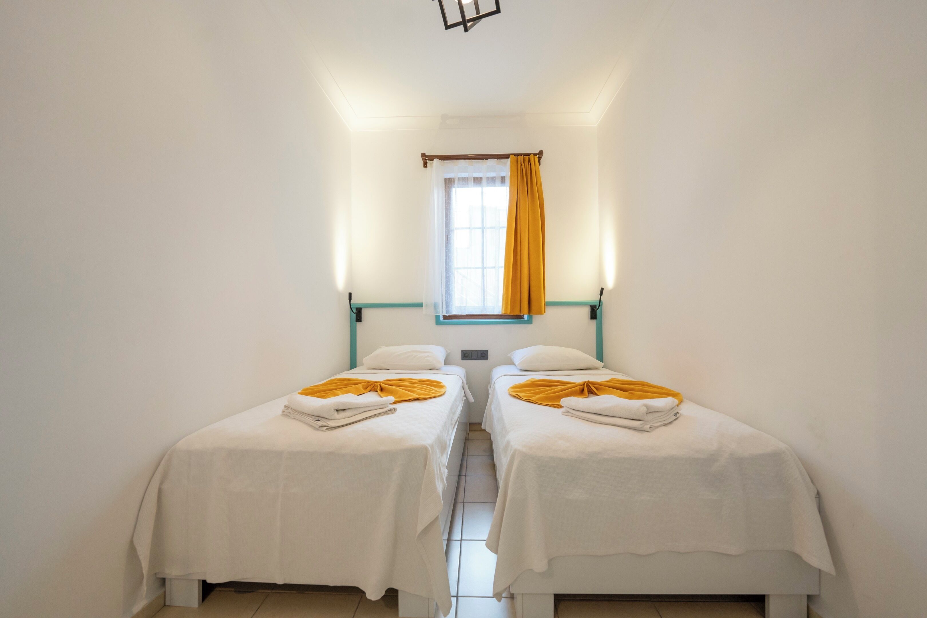 A room with two beds, white bedding, and a window with a yellow curtain.