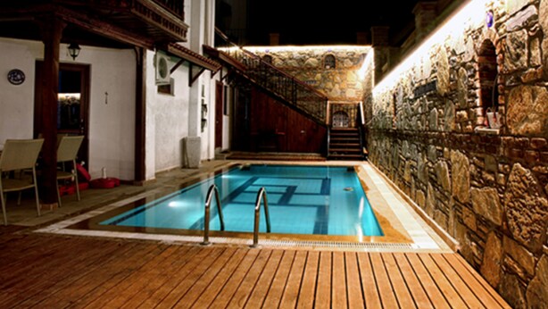 A swimming pool with wooden deck and stone walls, surrounded by a building with a balcony and stairs. - Ankakyaka Apart Hotel (Ula)