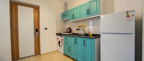 Una cocina con gabinetes color turquesa, una lavadora y un refrigerador blanco.