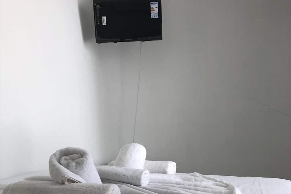 A hotel room with a bed, white towels, and a black wall-mounted TV.