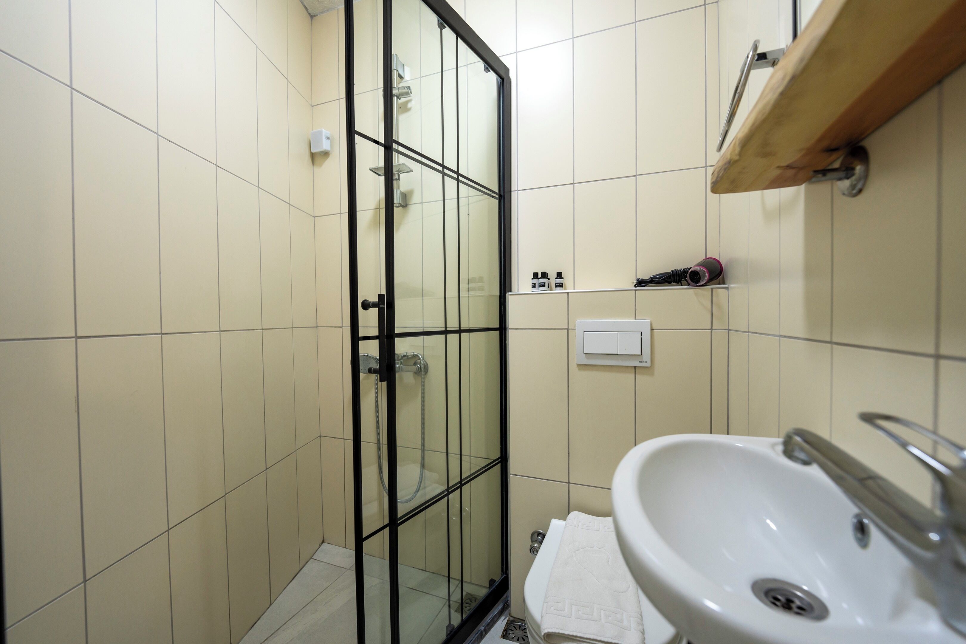 Et badeværelse med et glasafskærmet brusebad, en hvid vask og en hylde med toiletartikler.